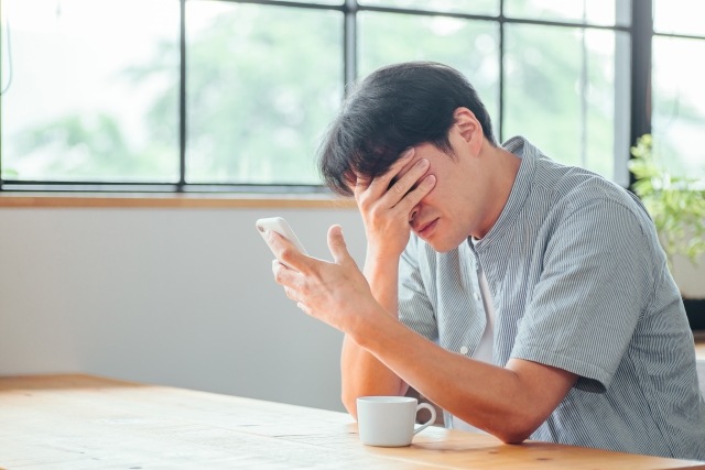 つながらない権利のアイキャッチ｜カフェでスマホを手に頭を抱える男性会社員。休日や勤務時間外の業務連絡にストレスを感じる様子を表現