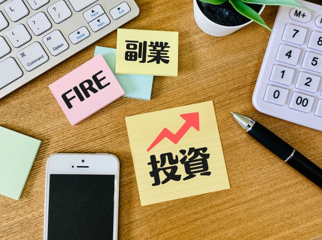 FIRE病のアイキャッチ｜「FIRE」「副業」「投資」と書かれた付箋と電卓・キーボード・スマホが並ぶデスク。上昇矢印が示す資産形成に取り憑かれる様子を象徴
