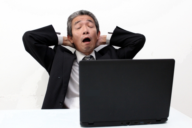 窓際族は勝ち組？のアイキャッチ｜スーツ姿の中高年男性がノートパソコンの前で両手を頭の後ろに組み、脱力してあくびをする様子。仕事に追われない窓際族の気楽な働き方を象徴