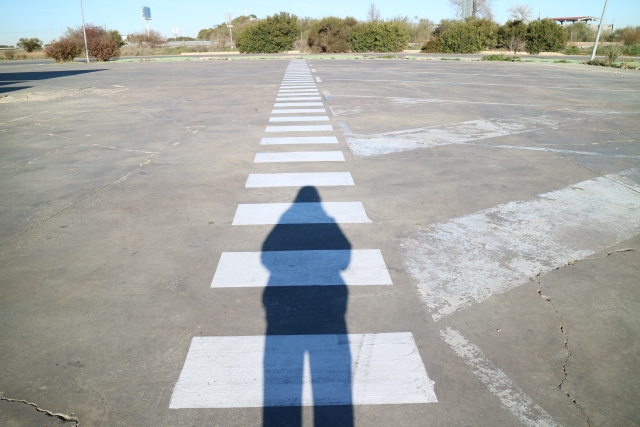 40代で人生詰んだと感じる人向け記事のアイキャッチ｜広い舗装路に白い破線がまっすぐ奥へ伸び、手前に立つ人の長い影が落ちている。行き止まりに見えて実はまだ道が続いていることを表現
