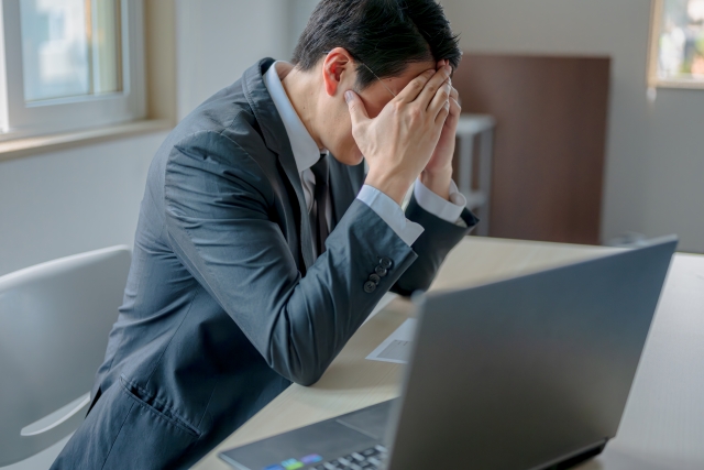 転職失敗で詰んだと感じる人向け記事のアイキャッチ｜スーツ姿の男性がノートパソコンの前で頭を抱え、両手で顔を覆ってうつむいている様子。転職先の現実に直面し、後悔や焦りを感じている心境を表現。